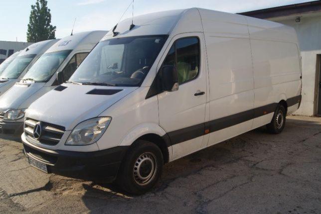 Rząd białych samochodów dostawczych Mercedes-Benz Sprinter, zaparkowanych na zewnątrz, z anteną na dachu i widocznym logo Mercedesa.