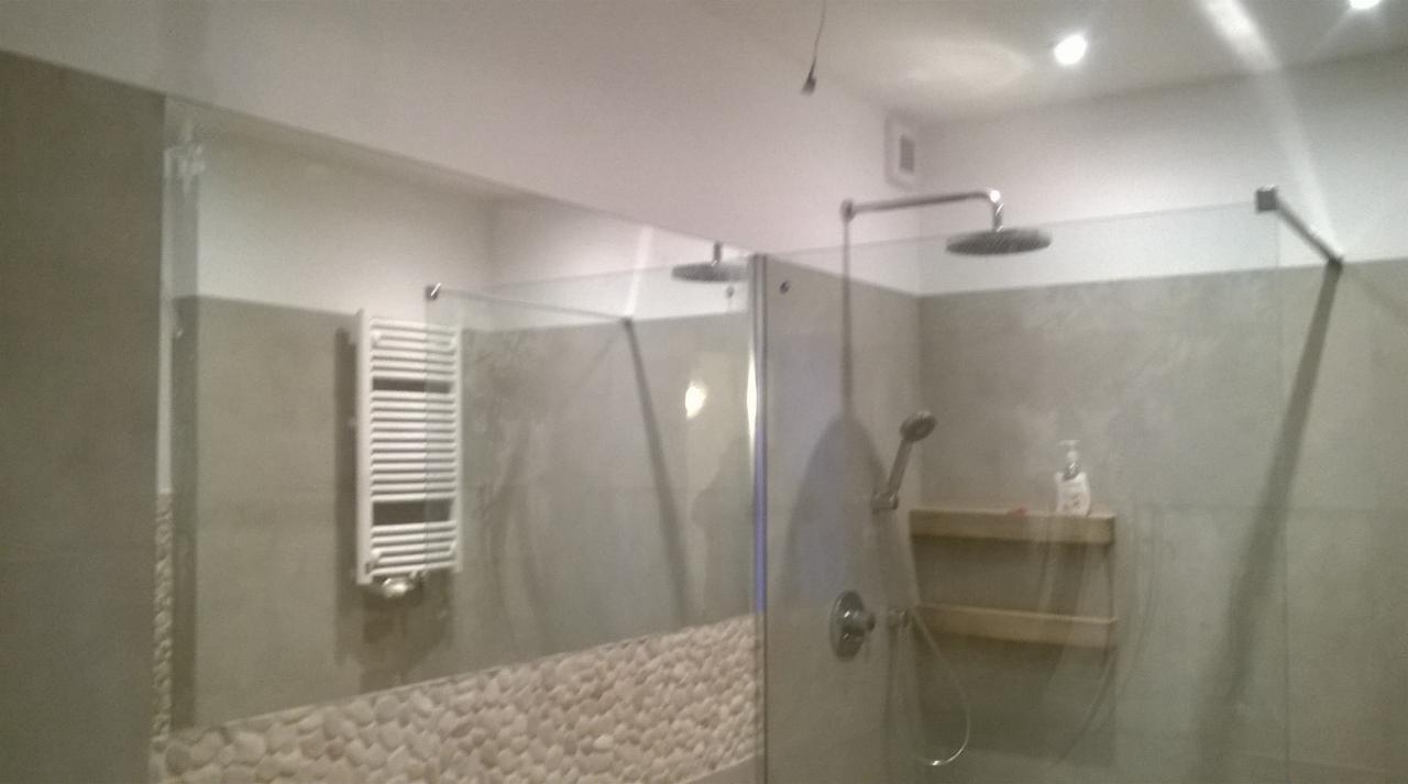 Szklana kabina prysznicowa z deszczownicą i półkami w wykończonej łazience z grzejnikiem drabinkowym i ścianą z kamyków.