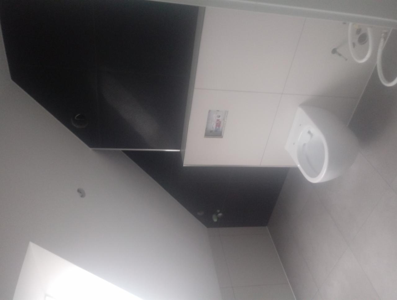 Nowoczesna łazienka z czarnym sufitem i białymi płytkami, widoczna wisząca toaleta i zabudowany system spłukiwania.