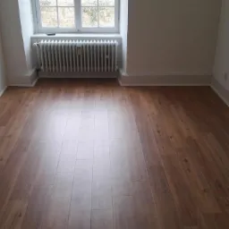 Nowo ułożone panele podłogowe w pustym, jasnym pokoju z grzejnikiem pod oknem.