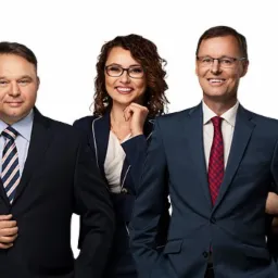 Zespół prawników w garniturach i koszulach, uśmiechnięci, ustawieni w rzędzie na białym tle.