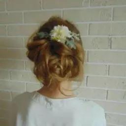 Upięcie włosów z kwiatową ozdobą na jasnym tle ceglanej ściany, widok z tyłu.