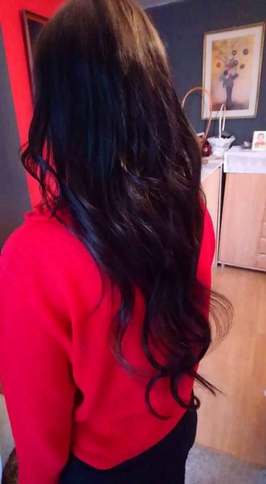 Długie, ciemne, pofalowane włosy, widok z tyłu, modelka w czerwonej bluzie, w tle komoda i obraz na ścianie.