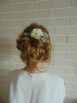 Upięcie włosów z kwiatową ozdobą na jasnym tle ceglanej ściany, widok z tyłu.