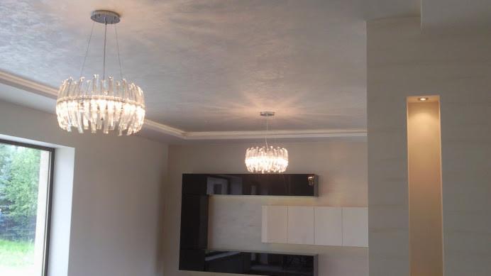 Jasne wnętrze z dwoma kryształowymi żyrandolami, dekoracyjną strukturą na suficie i ścianie oraz wnęką z oświetleniem punktowym