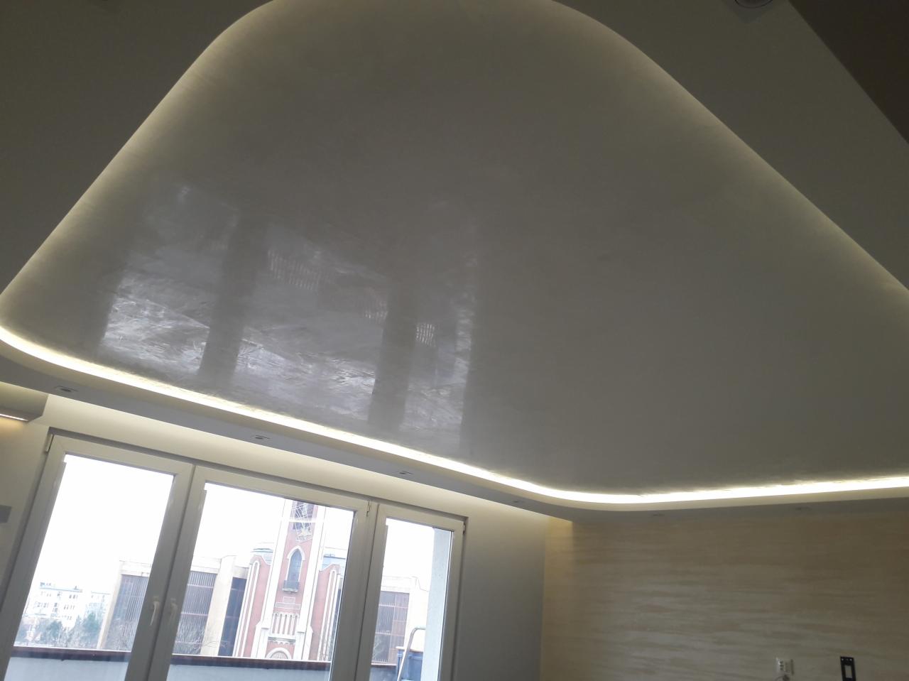Gładka, biała sufit podwieszany z zaokrąglonymi krawędziami i oświetleniem LED, odbijający światło z okien, z widokiem na budynek kościoła.
