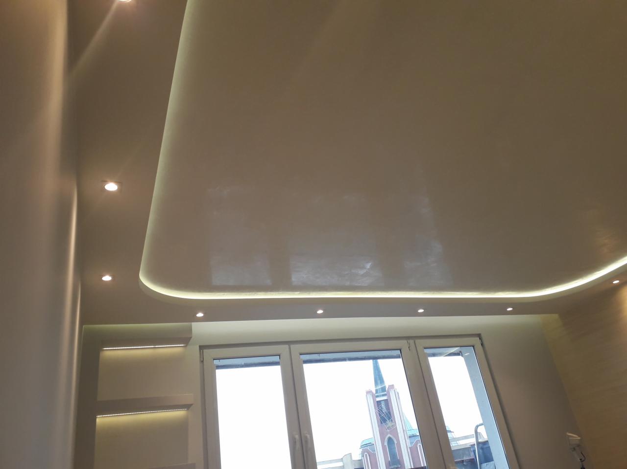 Podwieszany sufit z oświetleniem LED i punktowymi lampami, widok na kościół przez okno.
