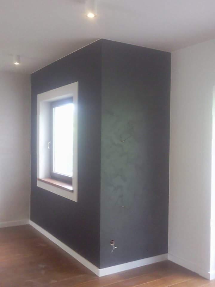 Pomieszczenie po świeżo wykonanych pracach: ściana pomalowana na ciemny kolor z widoczną fakturą, biała rama okienna i listwy przypodłogowe, drewniana podłoga, widoczne punkty świetlne na suficie.