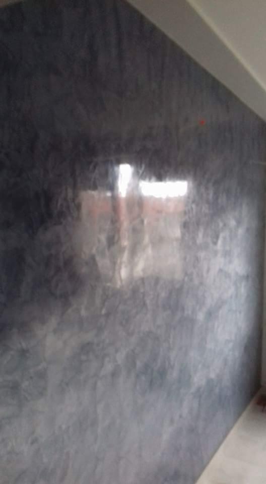 Ściana z efektem dekoracyjnym w odcieniach szarości, z widocznym odbiciem światła i fragmentem sufitu.