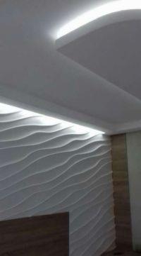 Ściana z dekoracyjnymi panelami 3D w kształcie fal, podświetlona listwą LED na suficie, tworząca nowoczesny efekt wizualny.