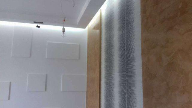 Nowoczesne wnętrze z akcentami: biała ściana z geometrycznymi panelami, tapeta w pionowe pasy i ściana w odcieniach brązu z efektem rustykalnym.