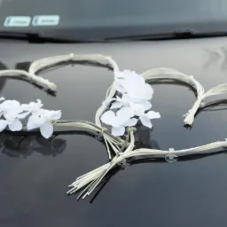 Dekoracja ślubna na samochodzie: dwa serca z białych kwiatów i rafii przymocowane przyssawkami do lakierowanej maski.