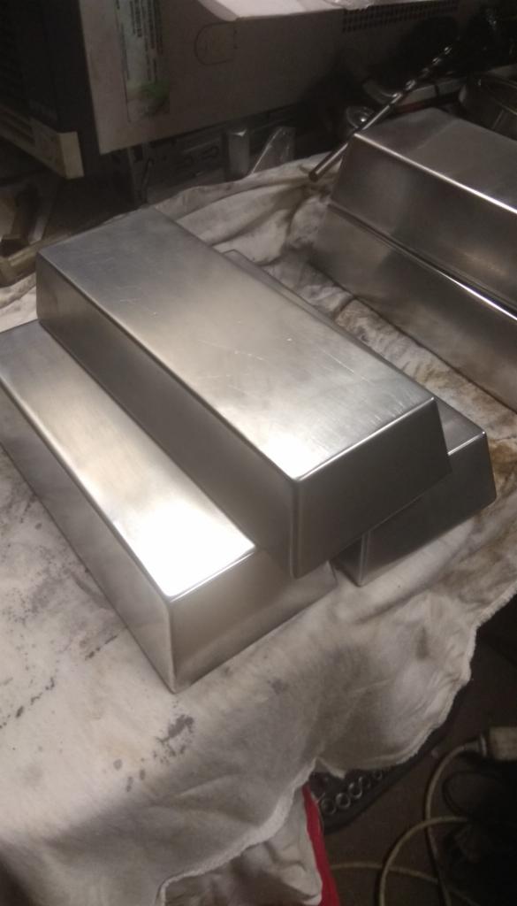 Szlifowane, prostokątne bloki metalu ułożone na brudnej szmacie, w tle widoczne narzędzia i wyposażenie warsztatowe.