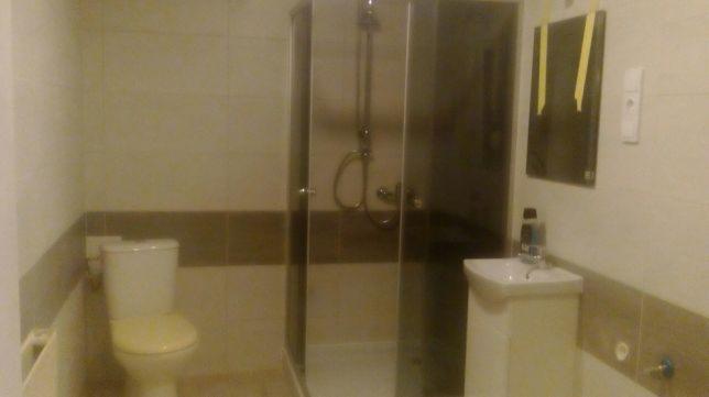 Ukończona łazienka z kabiną prysznicową, umywalką na szafce i toaletą. Na ścianie lustro zabezpieczone taśmą malarską.