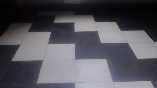 Ułożona podłoga z kwadratowych płytek w kolorze czarnym i białym, tworząca wzór szachownicy, z widocznymi fugami.