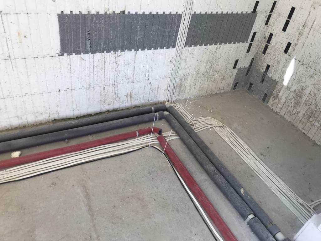 Surowy stan: Kable elektryczne ułożone wzdłuż ścian z betonu komórkowego, widoczne rury instalacyjne w izolacji, przed tynkowaniem.