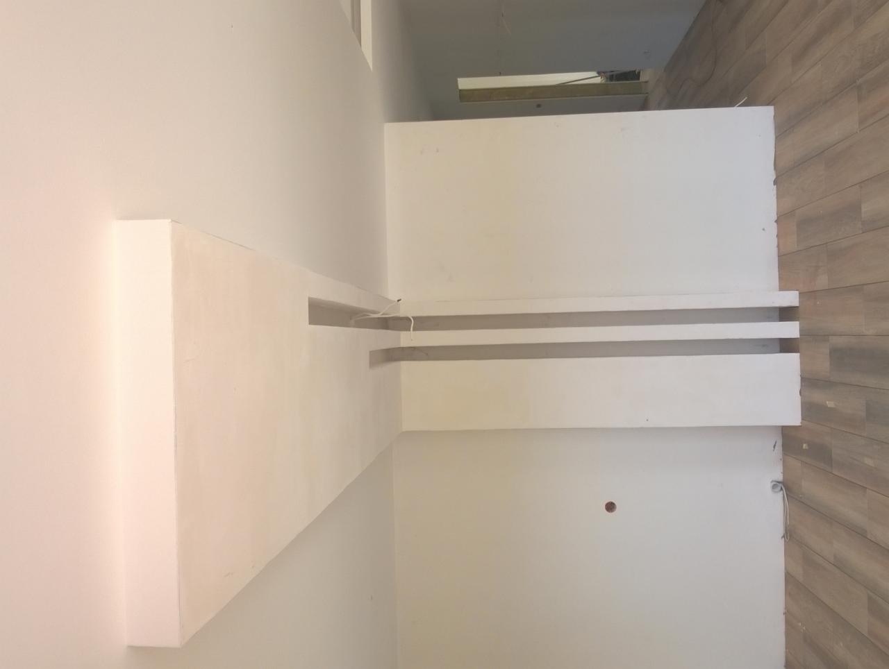 Niedokończona ściana z płyt kartonowo-gipsowych z wnękami na oświetlenie, widoczne przewody elektryczne, ściana wykończona płytkami imitującymi drewno.