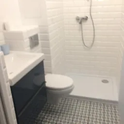 Nowoczesna łazienka z kabiną prysznicową wyłożoną białymi kafelkami typu 'metro', umywalką z szafką w kolorze granatowym i toaletą; podłoga w geometryczny wzór.