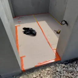 Wnętrze betonowej konstrukcji w trakcie budowy, zabezpieczone pomarańczową taśmą, z widocznymi kamieniami na zewnątrz i workiem na śmieci w środku.