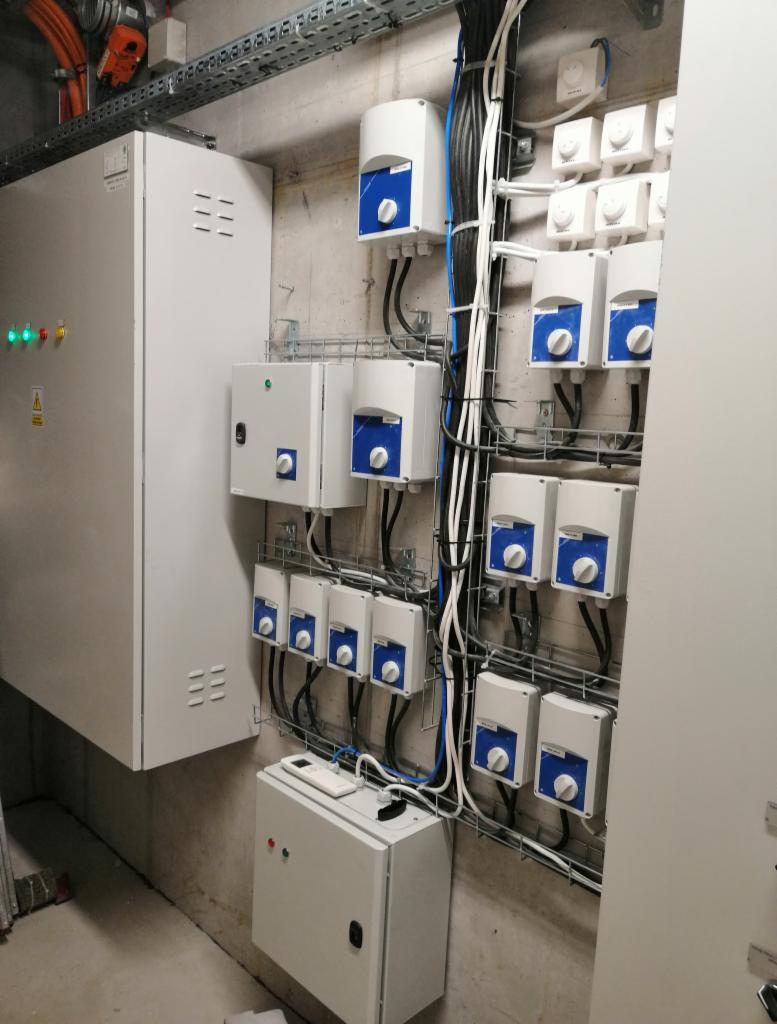 Rozdzielnica elektryczna z licznymi modułami zabezpieczającymi i okablowaniem, zamontowana na betonowej ścianie wewnątrz budynku.