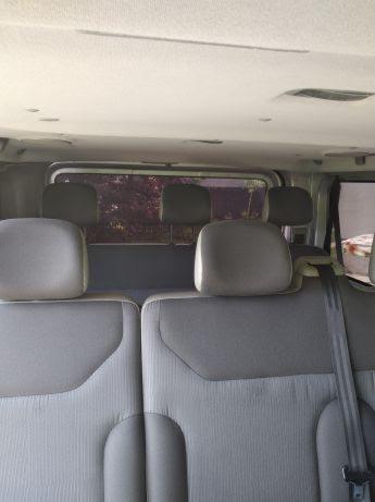 Wnętrze busa pasażerskiego z szarymi fotelami i widokiem na zewnątrz przez tylne okno.