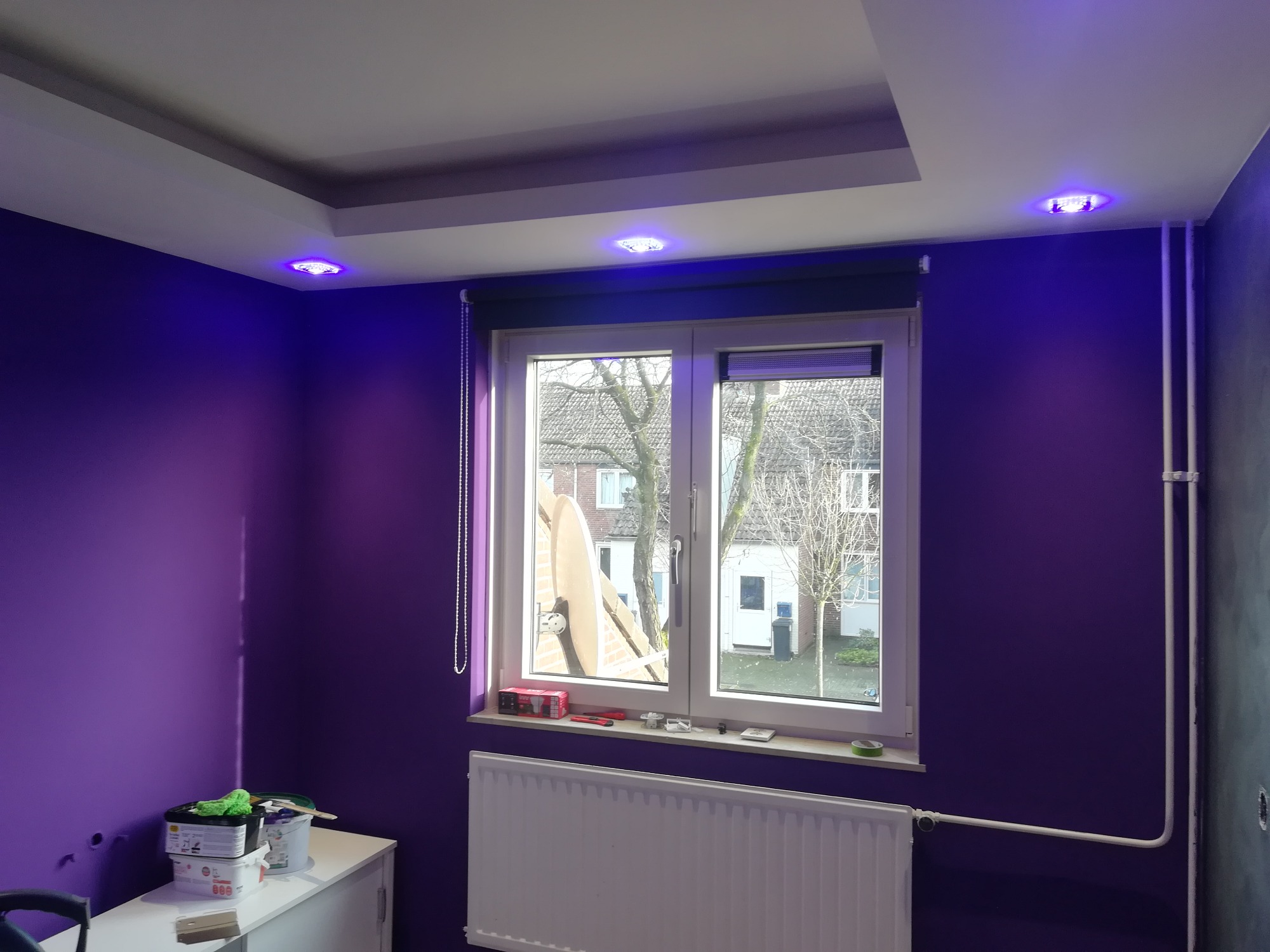 Fioletowy pokój po remoncie w Koninie z oświetleniem LED w suficie podwieszanym, widok na okno i grzejnik.
