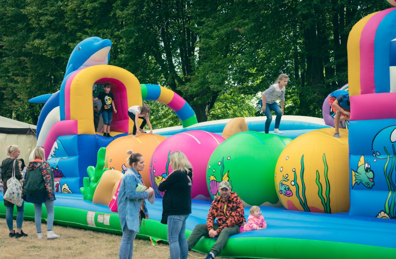 Dzieci bawią się na dmuchanym placu zabaw z motywem morskim, w tle drzewa i trawa.