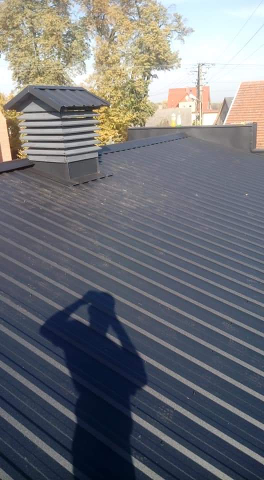 Nowe, ciemnoszare pokrycie dachowe z blachy trapezowej z kominkiem wentylacyjnym, cień fotografa na dachu.