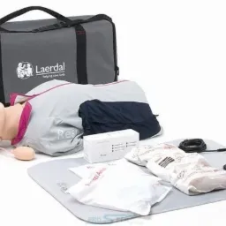 Manekin do ćwiczeń resuscytacji krążeniowo-oddechowej Laerdal na szarej macie, obok torba transportowa, pudełko z akcesoriami i kabel USB.