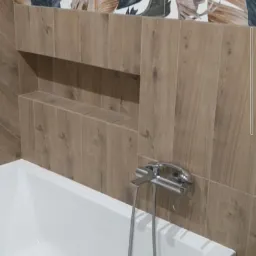 Nowoczesna łazienka z wanną, drewnopodobnymi płytkami i akcentem w postaci płytek z motywem liści bananowca nad wnęką w ścianie.