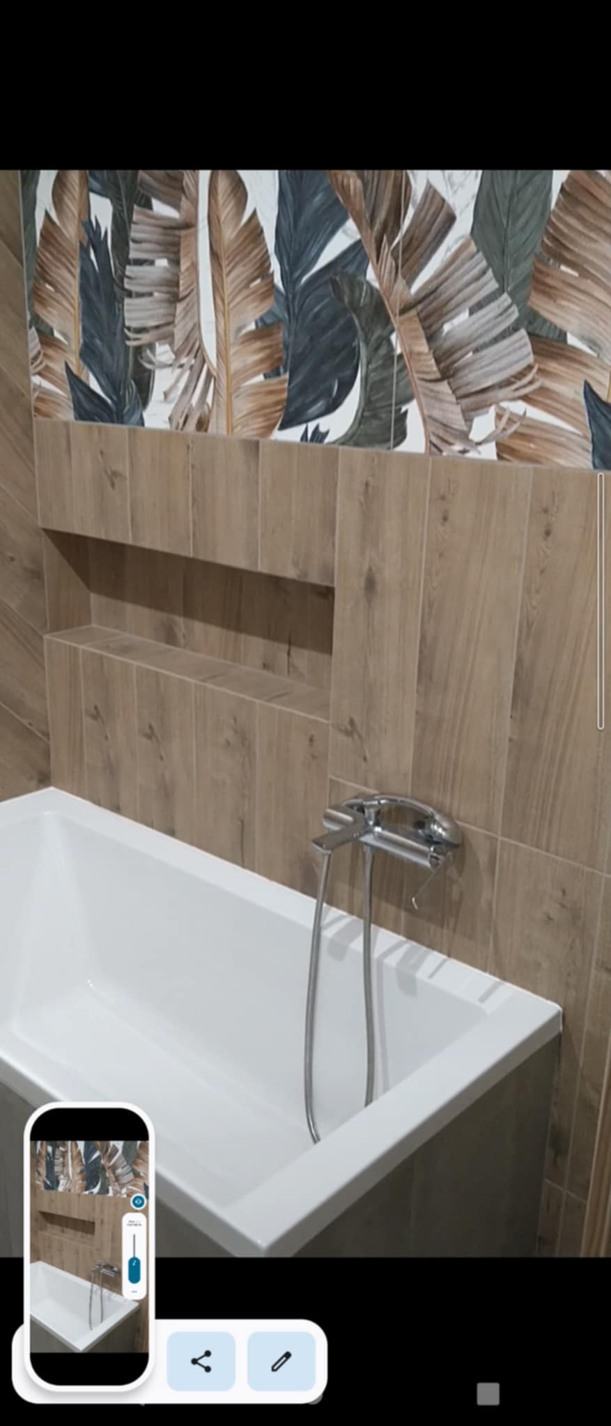 Nowoczesna łazienka z wanną, drewnopodobnymi płytkami i akcentem w postaci płytek z motywem liści bananowca nad wnęką w ścianie.