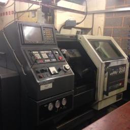 Krawmet - Tokarka CNC Colchester Tornado 350 w warsztacie z widocznym panelem sterowania i obudową, oświetlenie górne, ceglana ściana w tle.