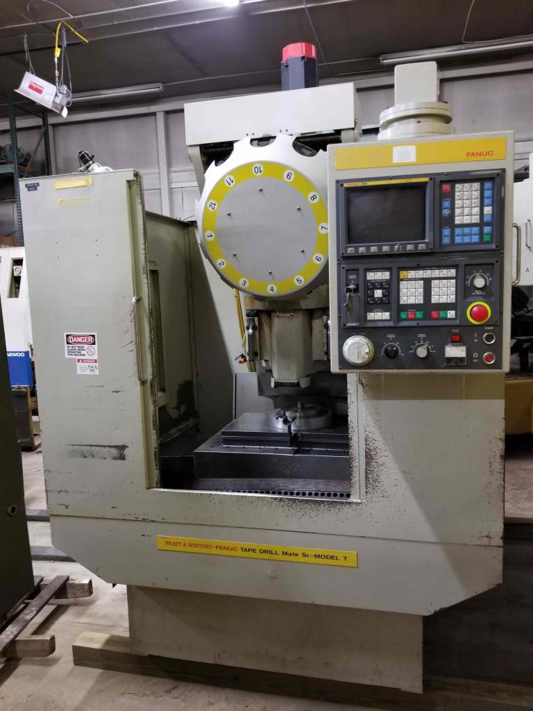 Przemysłowa wiertarka CNC Fanuc Tape Drill Mate Sr. Model T z tarczą indeksującą i panelem sterowania, widoczna tabliczka ostrzegawcza DANGER.