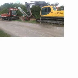 Dwa różne modele koparek: pomarańczowa i żółta, stojące obok siebie na żwirowej drodze, otoczone zielenią.