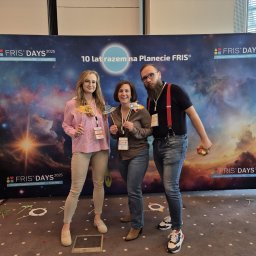 Circinus Training Center Adam Pluciński - Trzy osoby pozują z rekwizytami na tle baneru 'FRIS Days 2025'. Uczestnicy konferencji z kosmicznymi gadżetami. Uśmiechnięte twarze, wesoła atmosfera.