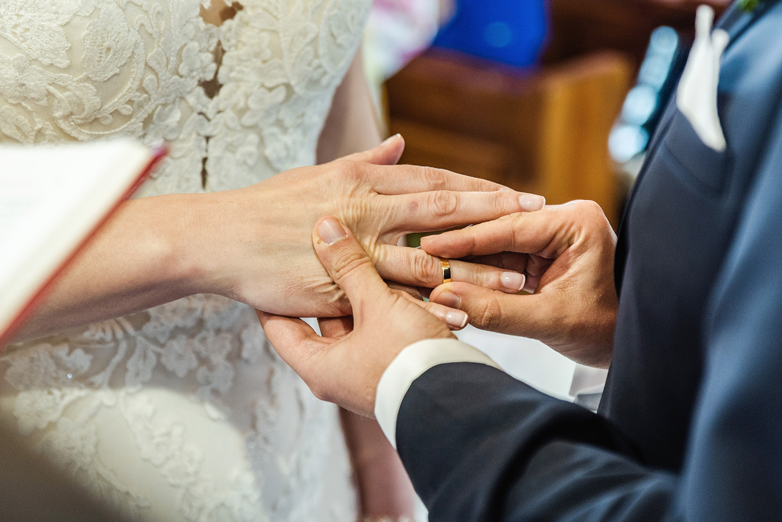 Moment zakładania złotej obrączki na palec panny młodej w koronkowej sukni ślubnej, zbliżenie dłoni.