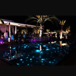 Oświetlony basen z gwiazdami w tle restauracji z palmami w nocy.