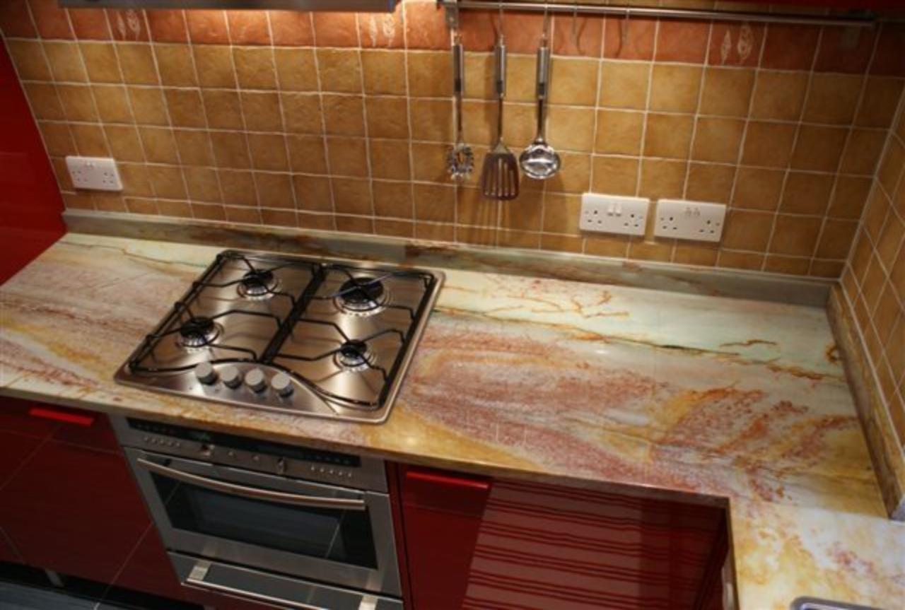 Kuchnia z blatem o unikalnym wzorze przypominającym marmur, z wbudowaną płytą grzewczą i piekarnikiem, na tle brązowych płytek.