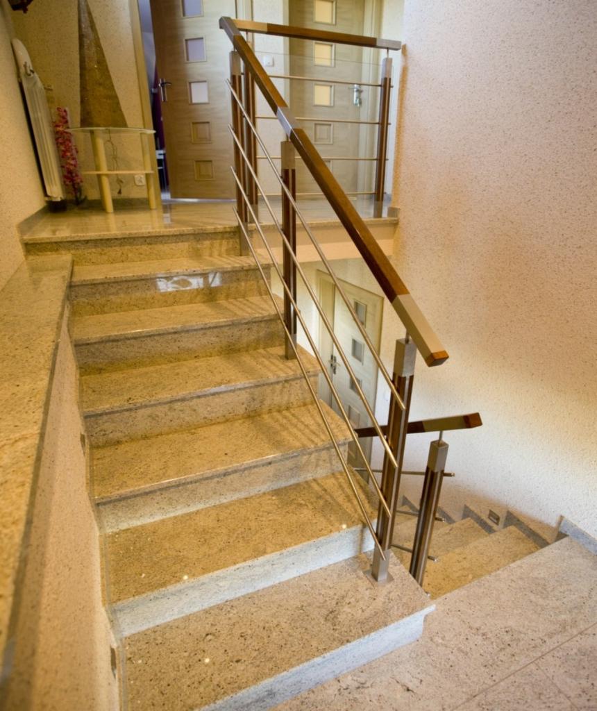 Wykończone schody wewnętrzne z jasnego kamienia z metalową balustradą z drewnianymi elementami, widok z góry.