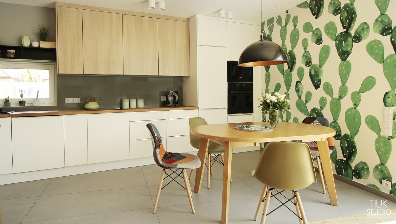 Jasna kuchnia z drewnianymi akcentami, okrągłym stołem i krzesłami Eames, ściana pokryta tapetą w kaktusy.