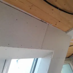 Montaż płyt na poddaszu z widocznymi łączeniami i drewnianym stropem z instalacją elektryczną.