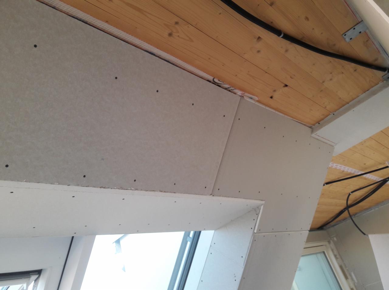 Montaż płyt na poddaszu z widocznymi łączeniami i drewnianym stropem z instalacją elektryczną.