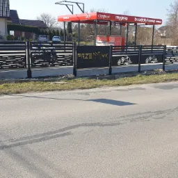 Nowoczesne, czarne ogrodzenie panelowe z ażurowymi wzorami i nazwą firmy na tle myjni bezdotykowej.