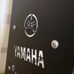 Czarny panel z wyciętymi laserowo logotypami Honda, Yamaha i Suzuki, przymocowany śrubami.