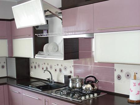 Nowoczesna kuchnia na wymiar w odcieniach lila i bieli, z szafką górną unoszoną do góry, czarnym blatem i płytą gazową z garnkiem i czajnikiem.