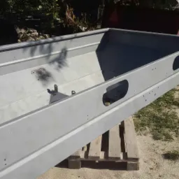 Wnętrze skrzyni ładunkowej przyczepy po odnowieniu, świeżo pomalowane na szaro, widoczne otwory i uchwyty, ustawione na palecie na zewnątrz.