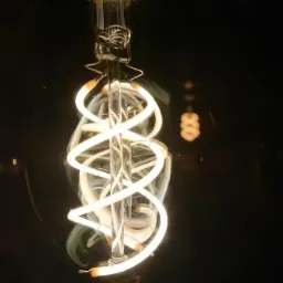 Żarówka LED z dekoracyjnym, spiralnym filamentem świecącym ciepłym światłem, widoczna na ciemnym tle.
