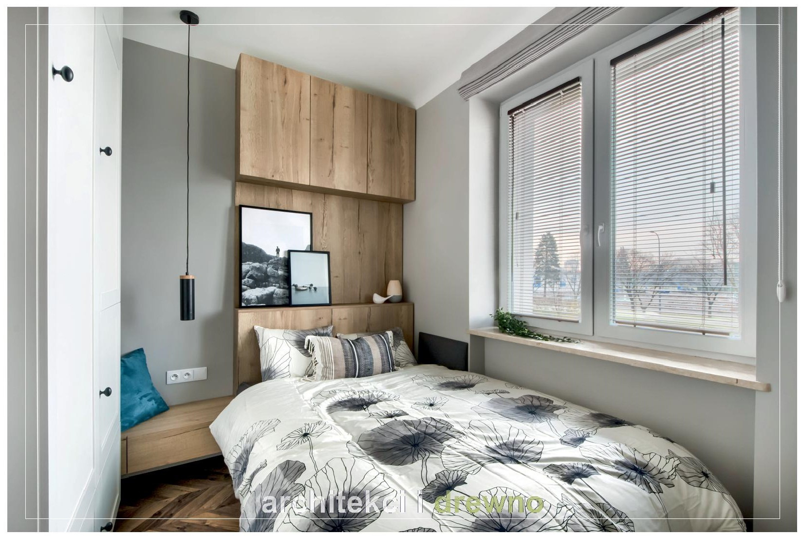 Nowoczesna sypialnia z łóżkiem w kwiaty, drewnianą zabudową nad wezgłowiem, wiszącą lampą i parkietem w jodełkę.