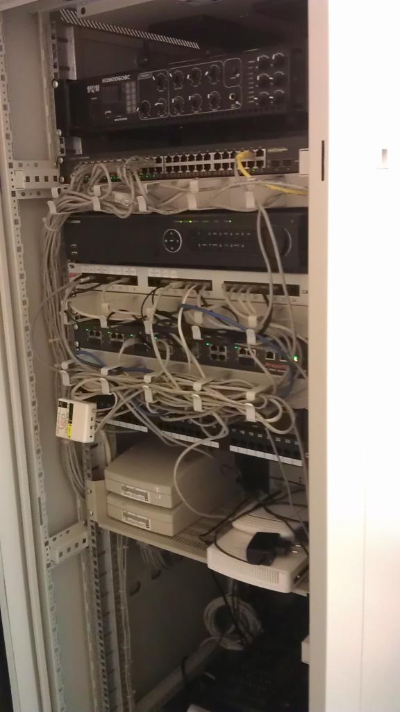 Szafa serwerowa z okablowaniem, przełącznikami sieciowymi i rejestratorem wideo, widoczne kable Ethernet i zasilające.