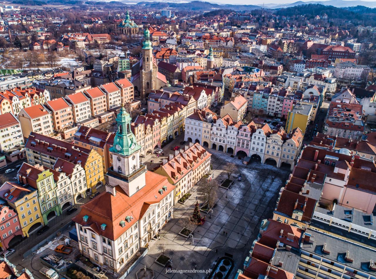 Panorama Jeleniej Góry z lotu ptaka, widok na rynek z kolorowymi kamienicami, zabytkową wieżą ratuszową i kościołem w tle.